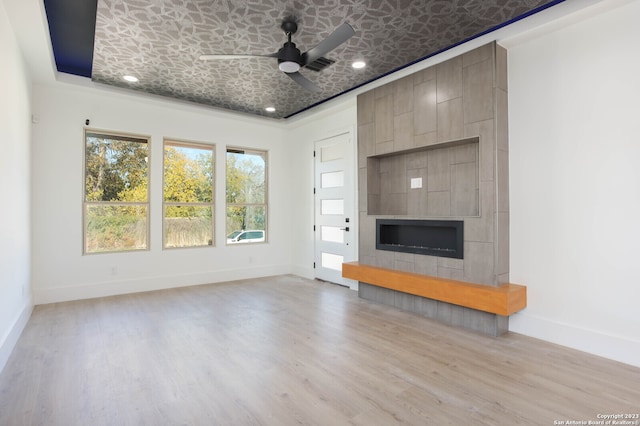 unfurnished living room featuring a large fireplace, ceiling fan, light hardwood / wood-style floors, and a tray ceiling