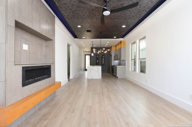 unfurnished living room with ceiling fan, plenty of natural light, a tile fireplace, and light hardwood / wood-style flooring