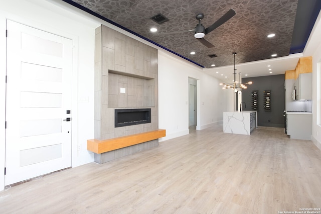 unfurnished living room featuring ceiling fan with notable chandelier, light hardwood / wood-style floors, and a fireplace