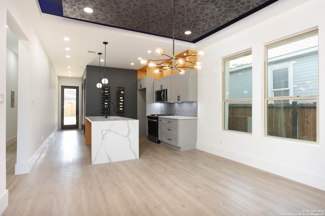 kitchen with light stone countertops, decorative backsplash, gray cabinetry, decorative light fixtures, and range with gas cooktop