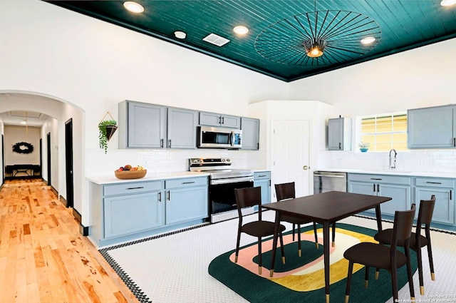 kitchen featuring appliances with stainless steel finishes, decorative light fixtures, light wood-type flooring, and decorative backsplash