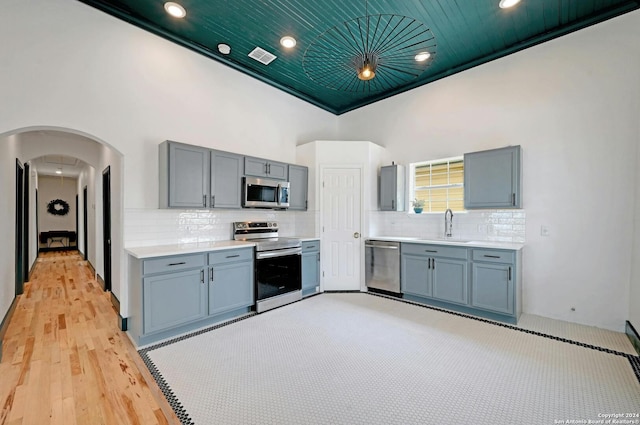 kitchen featuring appliances with stainless steel finishes, wooden ceiling, light wood-type flooring, a towering ceiling, and sink