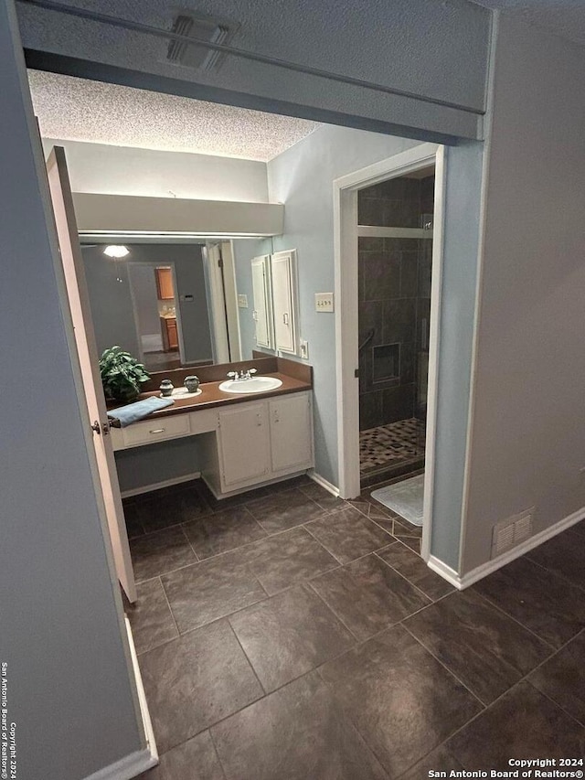 bathroom with tile patterned floors, a textured ceiling, vanity, and tiled shower