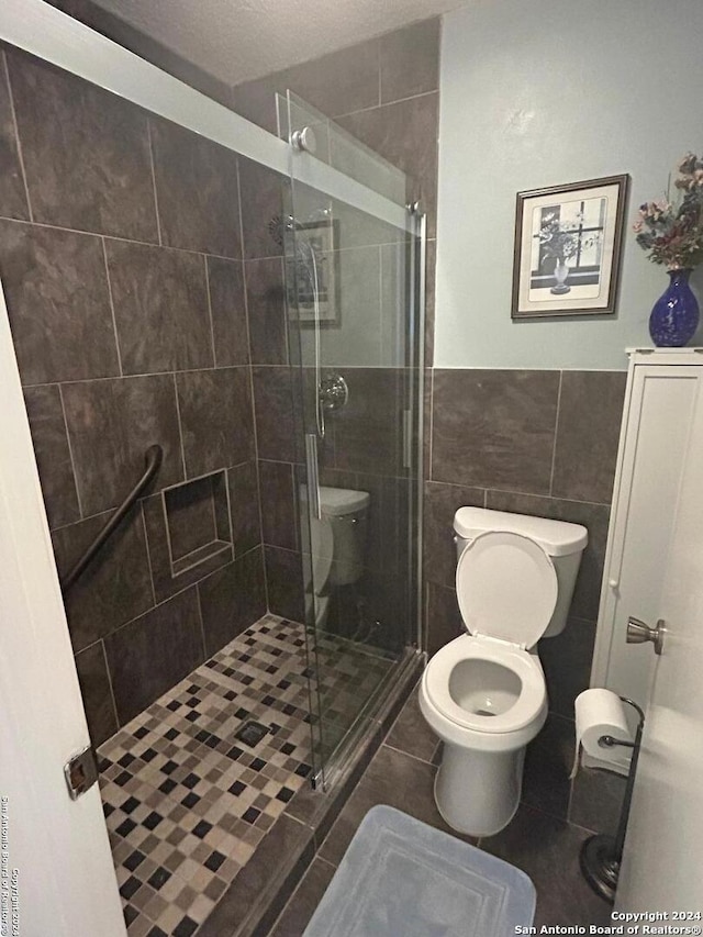 bathroom with a textured ceiling, tile walls, a shower with door, and toilet