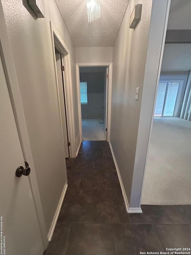 hallway with dark carpet and a textured ceiling