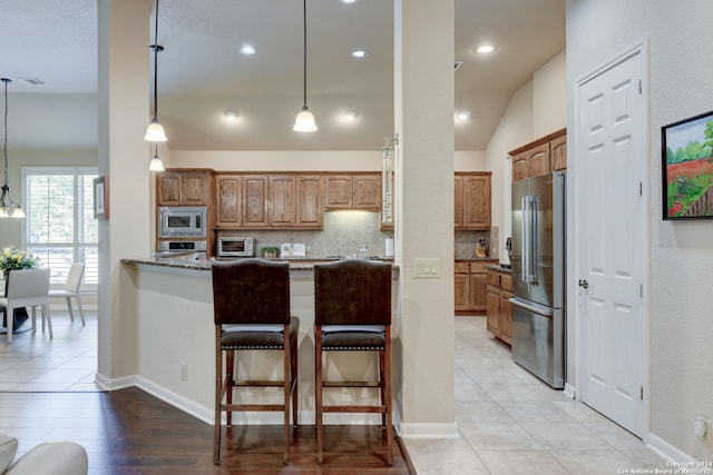 kitchen featuring decorative backsplash, hanging light fixtures, vaulted ceiling, appliances with stainless steel finishes, and stone countertops