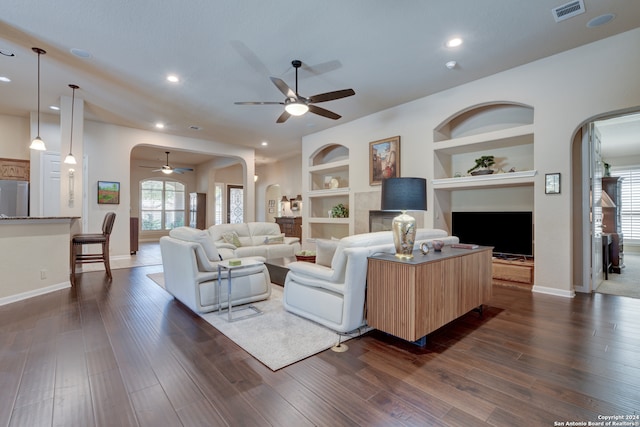 living room with plenty of natural light, built in shelves, dark hardwood / wood-style flooring, and ceiling fan