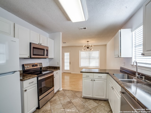 kitchen featuring sink, an inviting chandelier, a textured ceiling, white cabinets, and appliances with stainless steel finishes