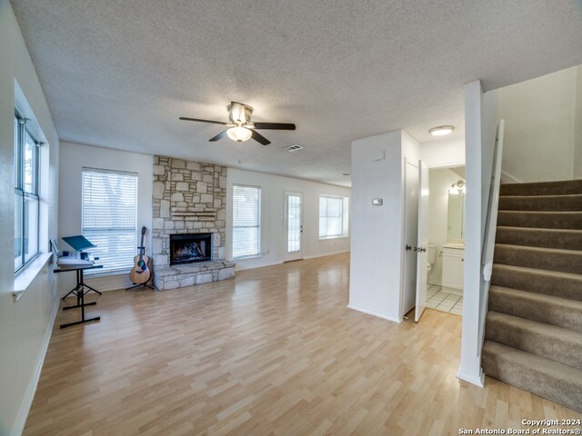 living room featuring ceiling fan, a stone fireplace, plenty of natural light, and light wood-type flooring