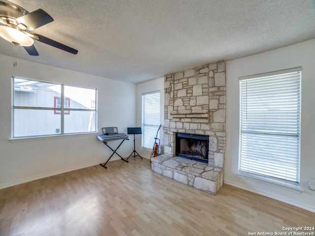 living room with ceiling fan, a stone fireplace, a textured ceiling, and light hardwood / wood-style flooring