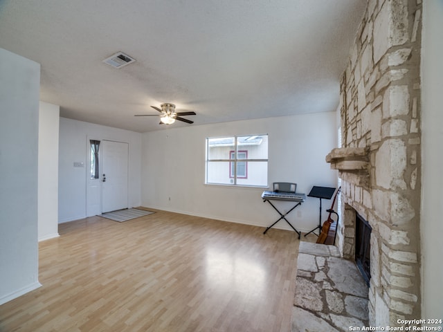 unfurnished living room featuring ceiling fan, a fireplace, a textured ceiling, and light wood-type flooring