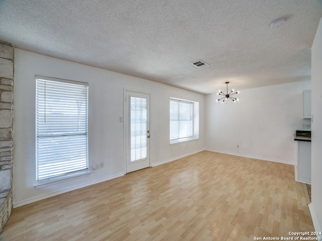 unfurnished living room featuring light hardwood / wood-style floors, a textured ceiling, and a chandelier