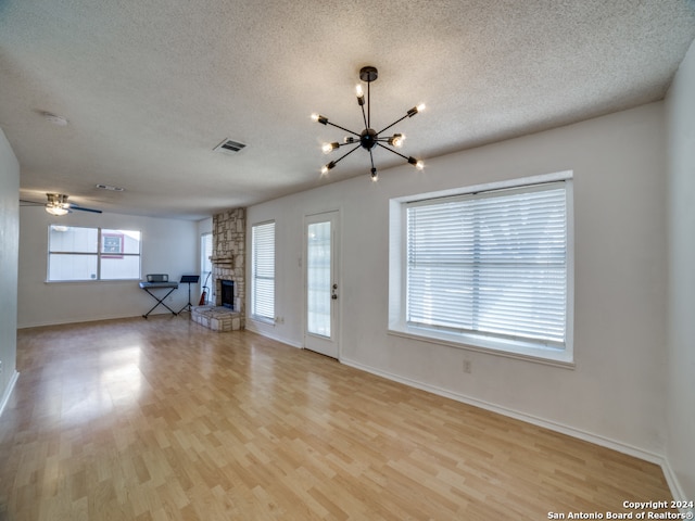 unfurnished living room with a textured ceiling, ceiling fan with notable chandelier, light wood-type flooring, and a fireplace