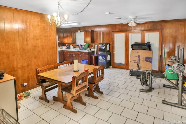 dining space featuring ceiling fan with notable chandelier and wood walls