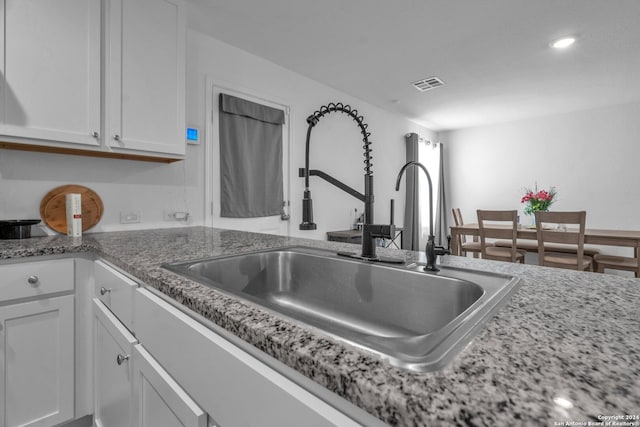 kitchen with light stone counters, sink, and white cabinetry