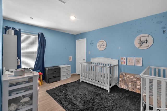 bedroom featuring wood-type flooring and a nursery area