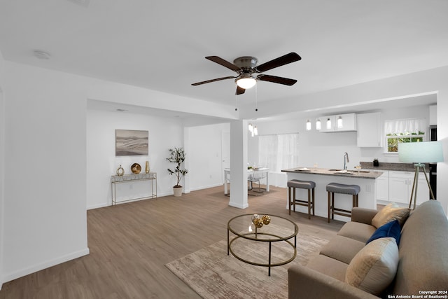 living room featuring ceiling fan with notable chandelier, light hardwood / wood-style floors, and sink