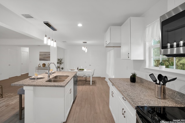 kitchen with pendant lighting, white cabinets, sink, a center island with sink, and appliances with stainless steel finishes