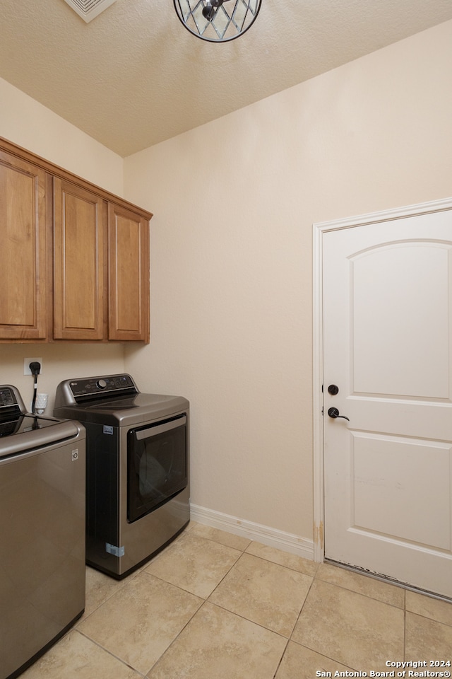 clothes washing area with cabinets, a textured ceiling, washing machine and dryer, and light tile patterned flooring