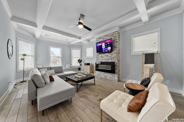 living room with beam ceiling, coffered ceiling, light hardwood / wood-style flooring, a stone fireplace, and ceiling fan