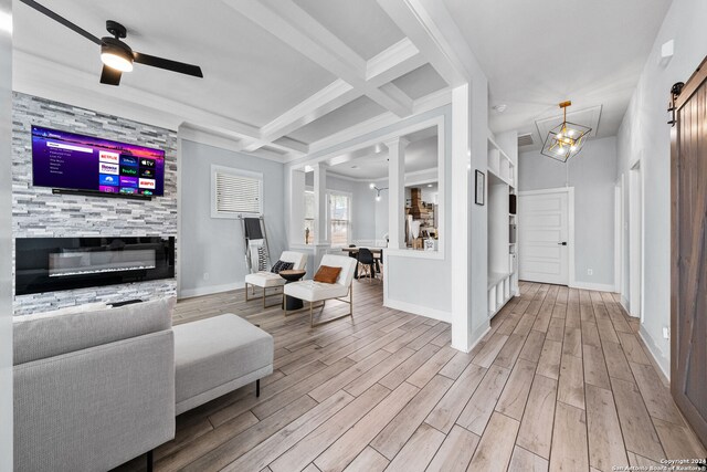 living room featuring ceiling fan, beamed ceiling, light hardwood / wood-style floors, decorative columns, and a barn door