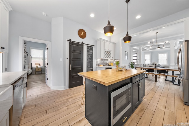 kitchen featuring appliances with stainless steel finishes, white cabinets, a barn door, a kitchen island, and a wealth of natural light