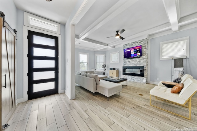 living room featuring a barn door, beam ceiling, a stone fireplace, and light wood-type flooring