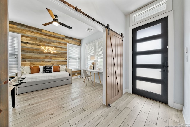 entrance foyer with wooden walls, ceiling fan, light wood-type flooring, and a barn door