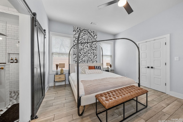 bedroom featuring light wood-type flooring, ceiling fan, multiple windows, and a barn door