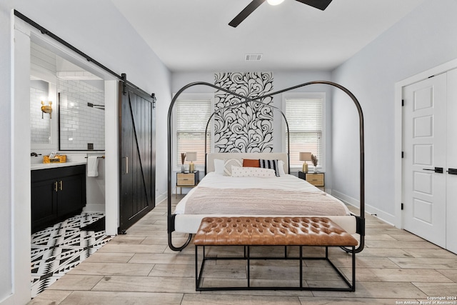 bedroom featuring ceiling fan, light hardwood / wood-style flooring, connected bathroom, and a barn door