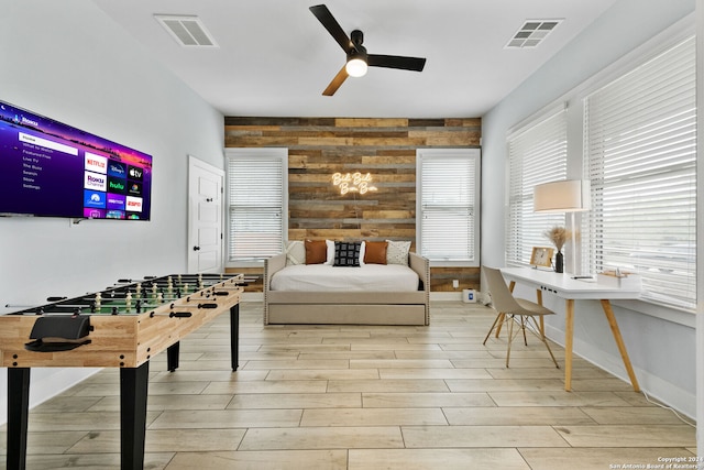 bedroom featuring light hardwood / wood-style floors, wooden walls, and ceiling fan