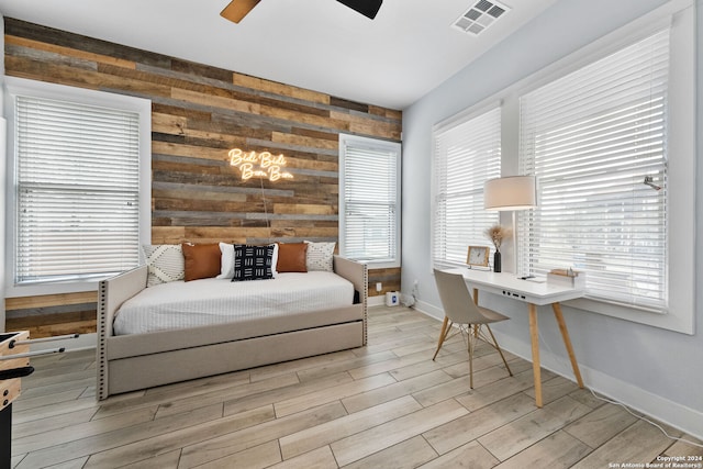 bedroom featuring multiple windows, light wood-type flooring, wooden walls, and ceiling fan