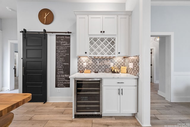 bar featuring tasteful backsplash, beverage cooler, white cabinetry, light wood-type flooring, and a barn door