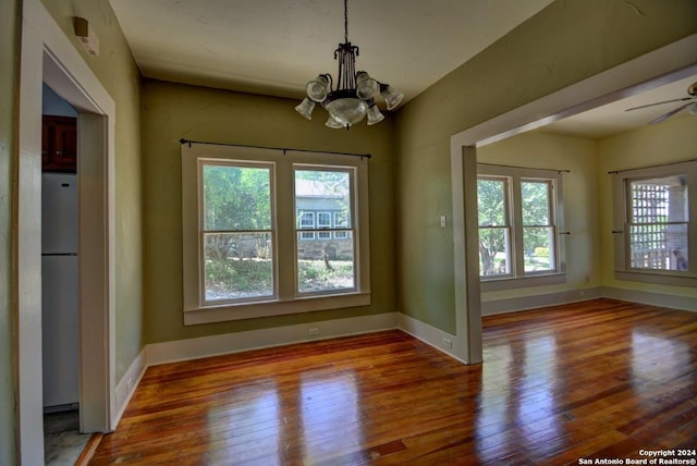 unfurnished dining area with wood-type flooring and ceiling fan with notable chandelier