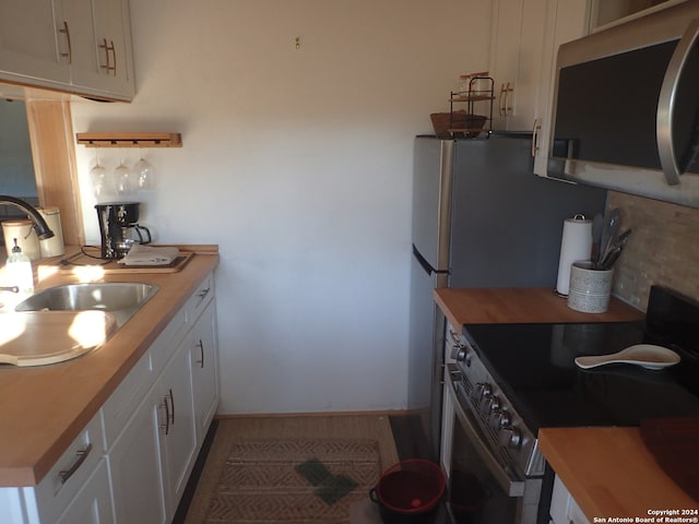 kitchen with appliances with stainless steel finishes, sink, wooden counters, and white cabinets