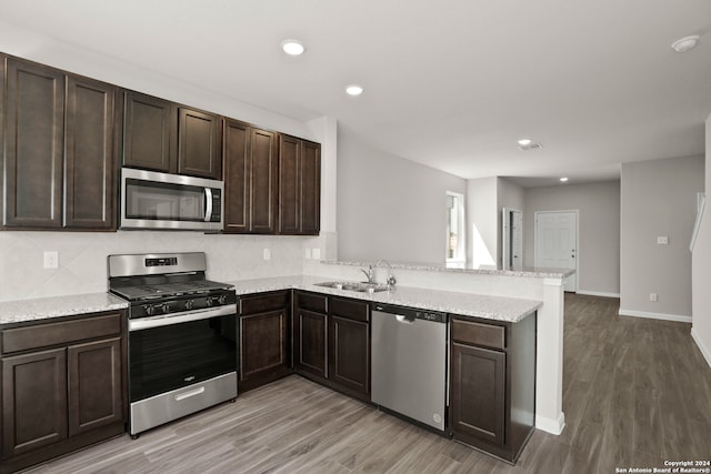 kitchen with dark brown cabinetry, appliances with stainless steel finishes, light hardwood / wood-style floors, and kitchen peninsula