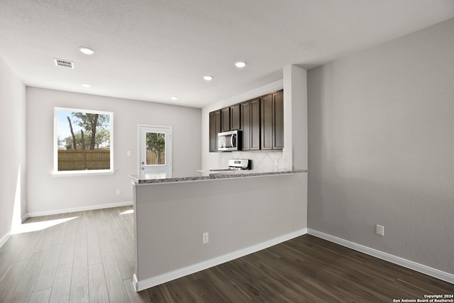 kitchen with light stone counters, dark brown cabinetry, kitchen peninsula, white range oven, and dark hardwood / wood-style flooring