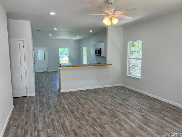 unfurnished living room featuring a textured ceiling, ceiling fan, and dark wood-type flooring