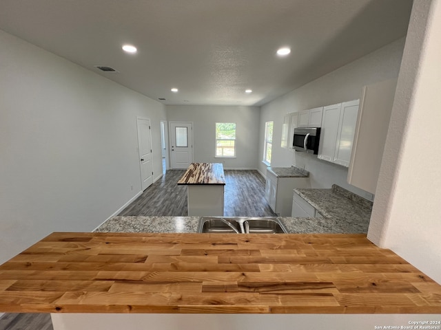 kitchen featuring wood-type flooring, butcher block countertops, sink, and white cabinetry