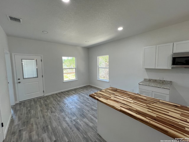 kitchen with white cabinets, a textured ceiling, light hardwood / wood-style floors, and butcher block counters