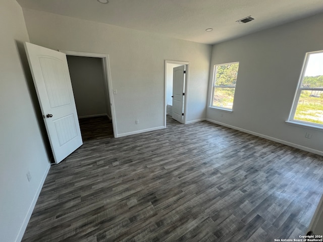 unfurnished bedroom with dark hardwood / wood-style floors, multiple windows, and a spacious closet