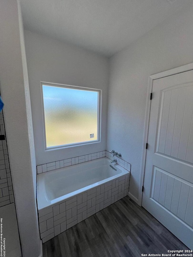 bathroom with wood-type flooring and a relaxing tiled tub