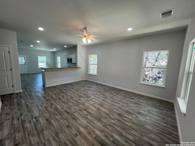 unfurnished living room featuring dark wood-type flooring, ceiling fan, and a healthy amount of sunlight