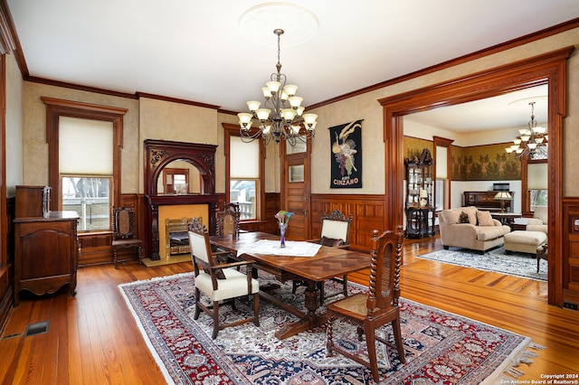 dining room featuring wood-type flooring, a fireplace, crown molding, and a chandelier