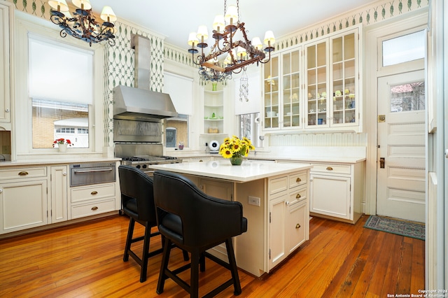 kitchen with a kitchen breakfast bar, wall chimney exhaust hood, pendant lighting, a center island, and hardwood / wood-style floors