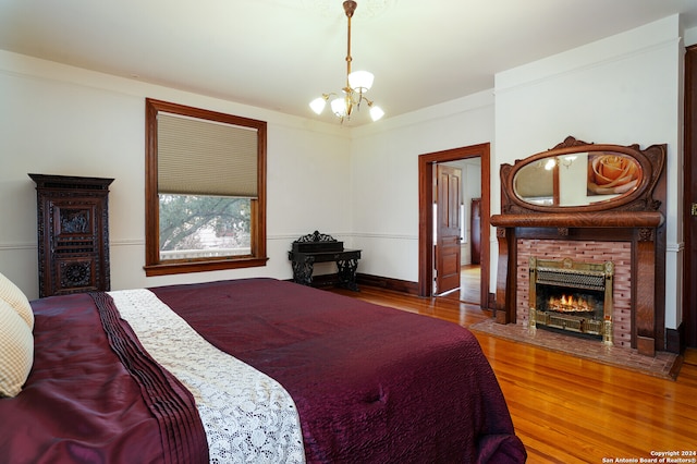 bedroom featuring crown molding, a chandelier, a brick fireplace, and hardwood / wood-style flooring