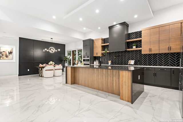 kitchen with custom exhaust hood, an island with sink, decorative light fixtures, and decorative backsplash