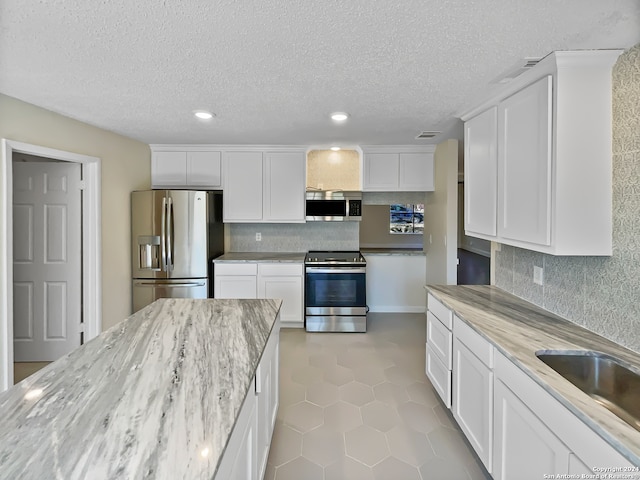 kitchen featuring appliances with stainless steel finishes, a textured ceiling, white cabinetry, and light tile patterned floors