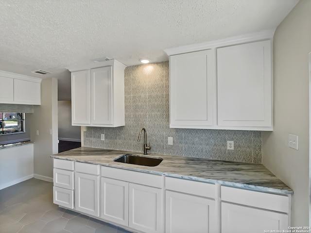 kitchen with light tile patterned flooring, a textured ceiling, sink, and white cabinetry