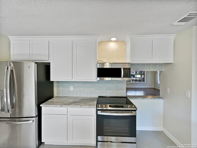 kitchen featuring light stone countertops, a textured ceiling, stainless steel appliances, and white cabinetry